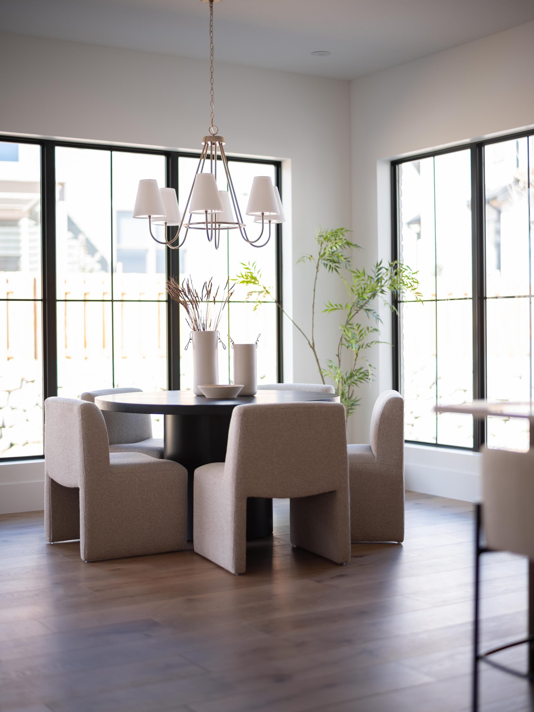 Dining table beneath a black chandelier with tall windows
