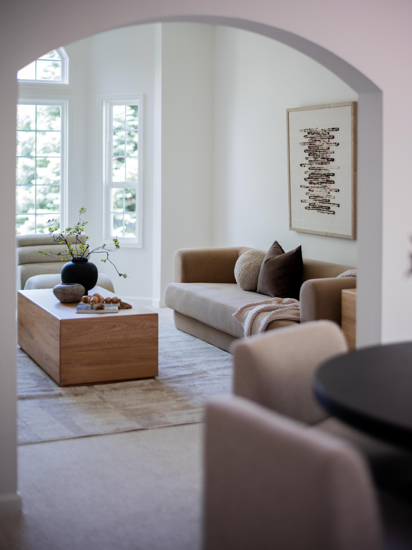 Staged living room viewed through an arched doorway, oak table and bouclé seating