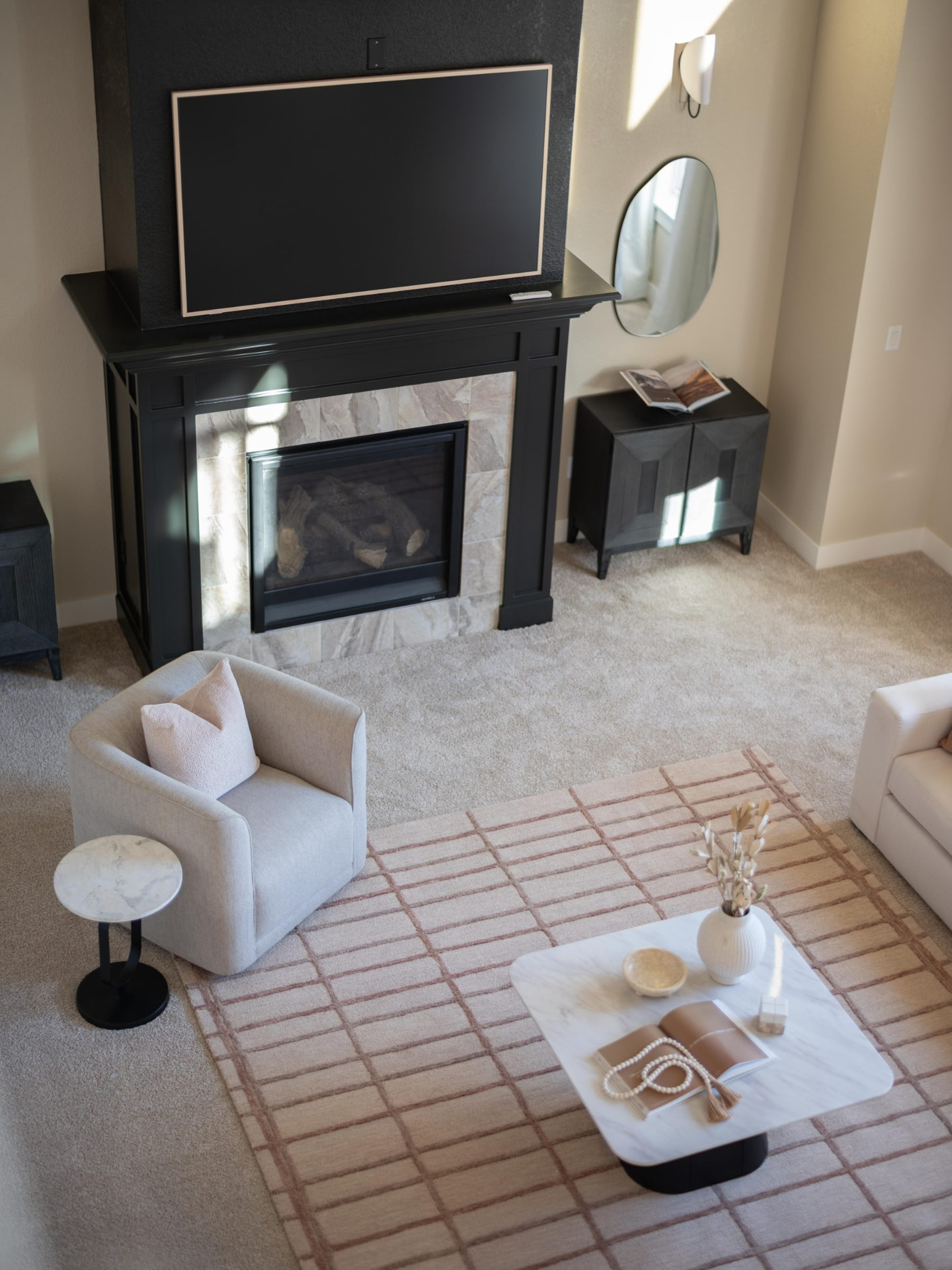 Living room seen from above with a black mantel fireplace, cream swivel chair and marble coffee table on a rose-lined rug