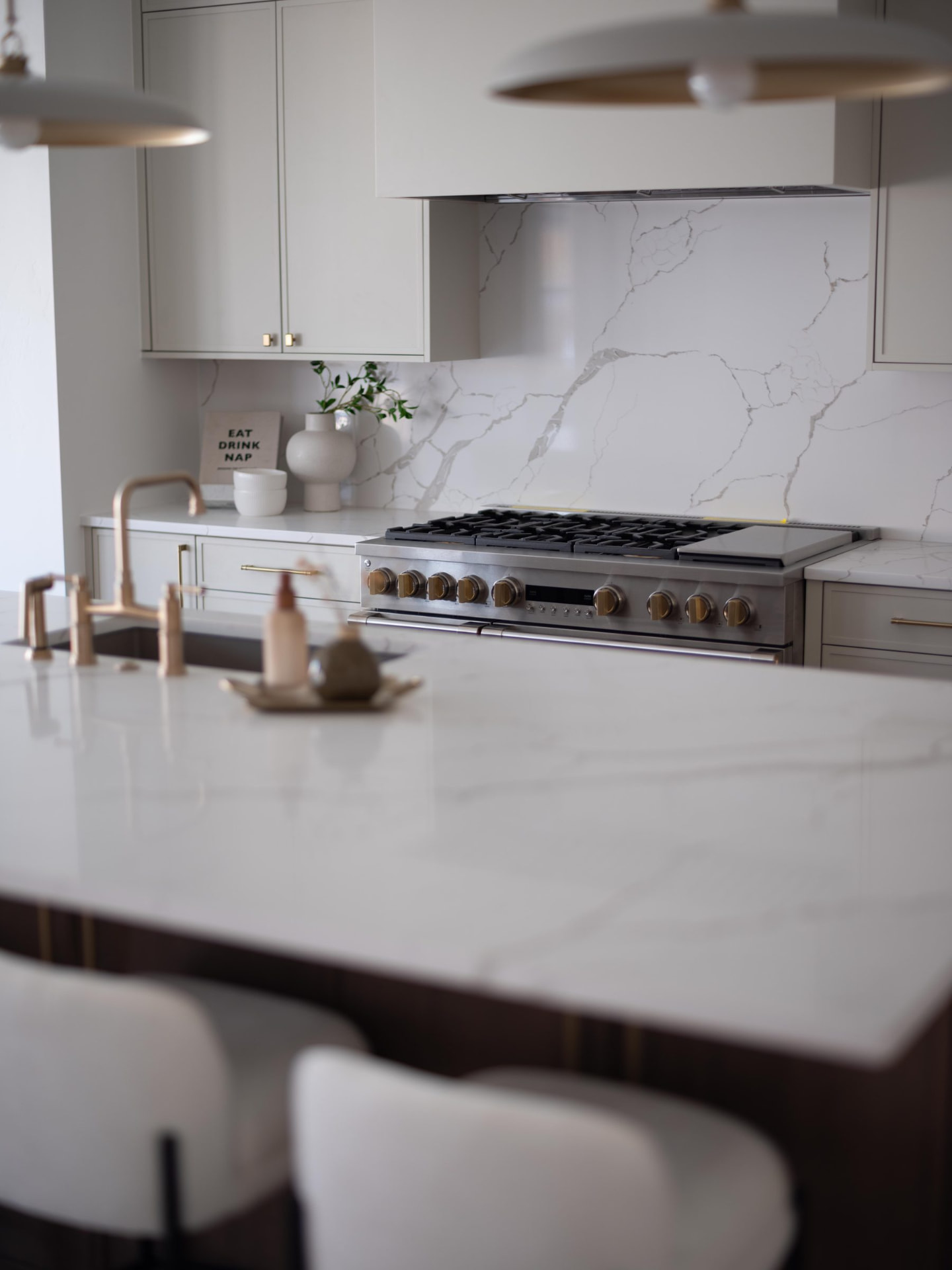 Kitchen island in marble with a professional range, waterfall backsplash and warm brass pendants overhead
