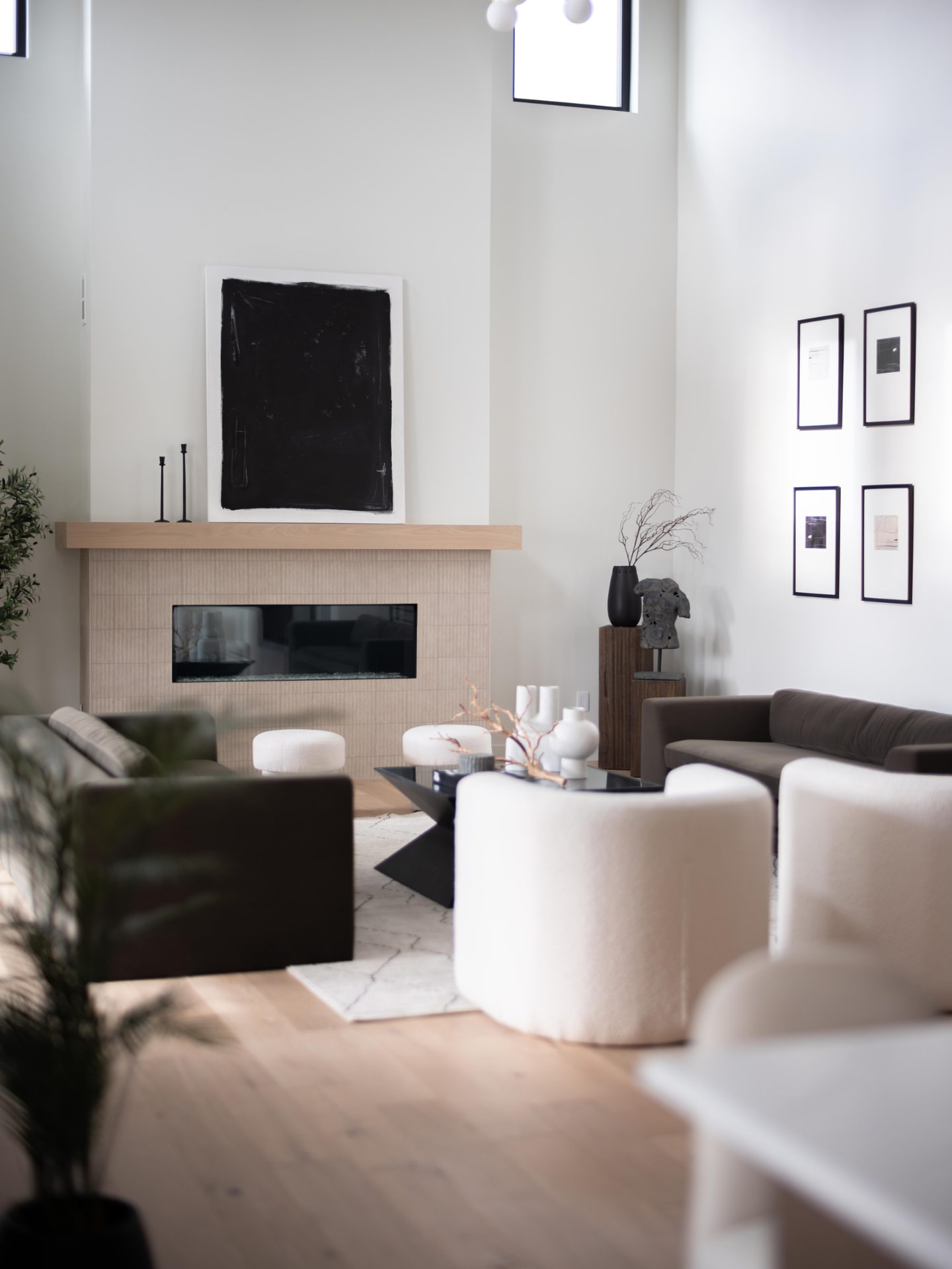 Double-height living room with a black abstract canvas above a pale tile fireplace and curved bouclé seating