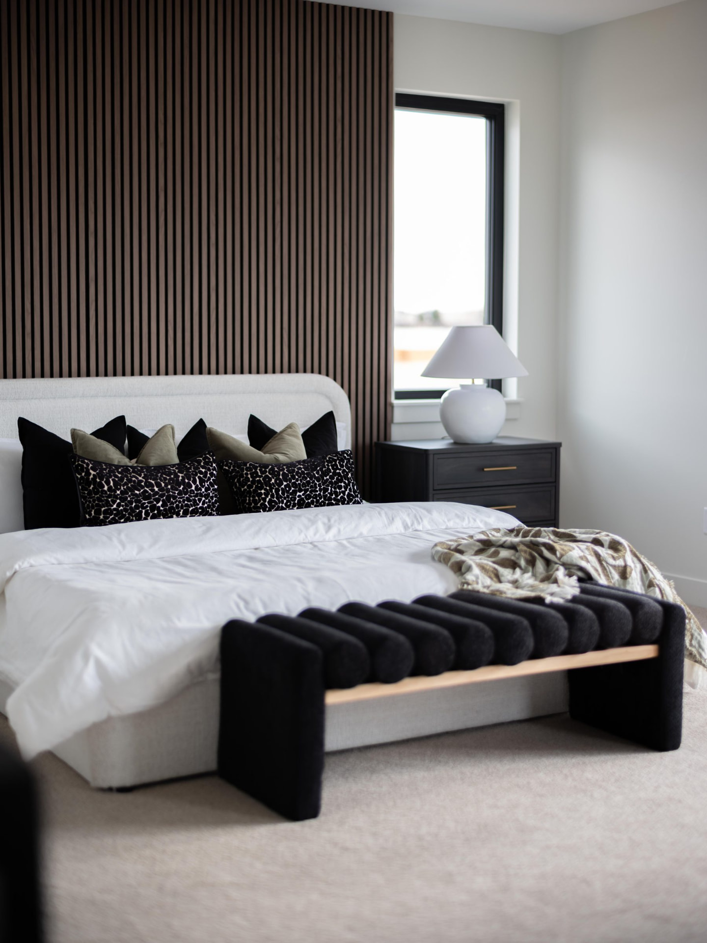 Primary bedroom with a walnut slat accent wall, upholstered bed and a channelled black bench at the foot