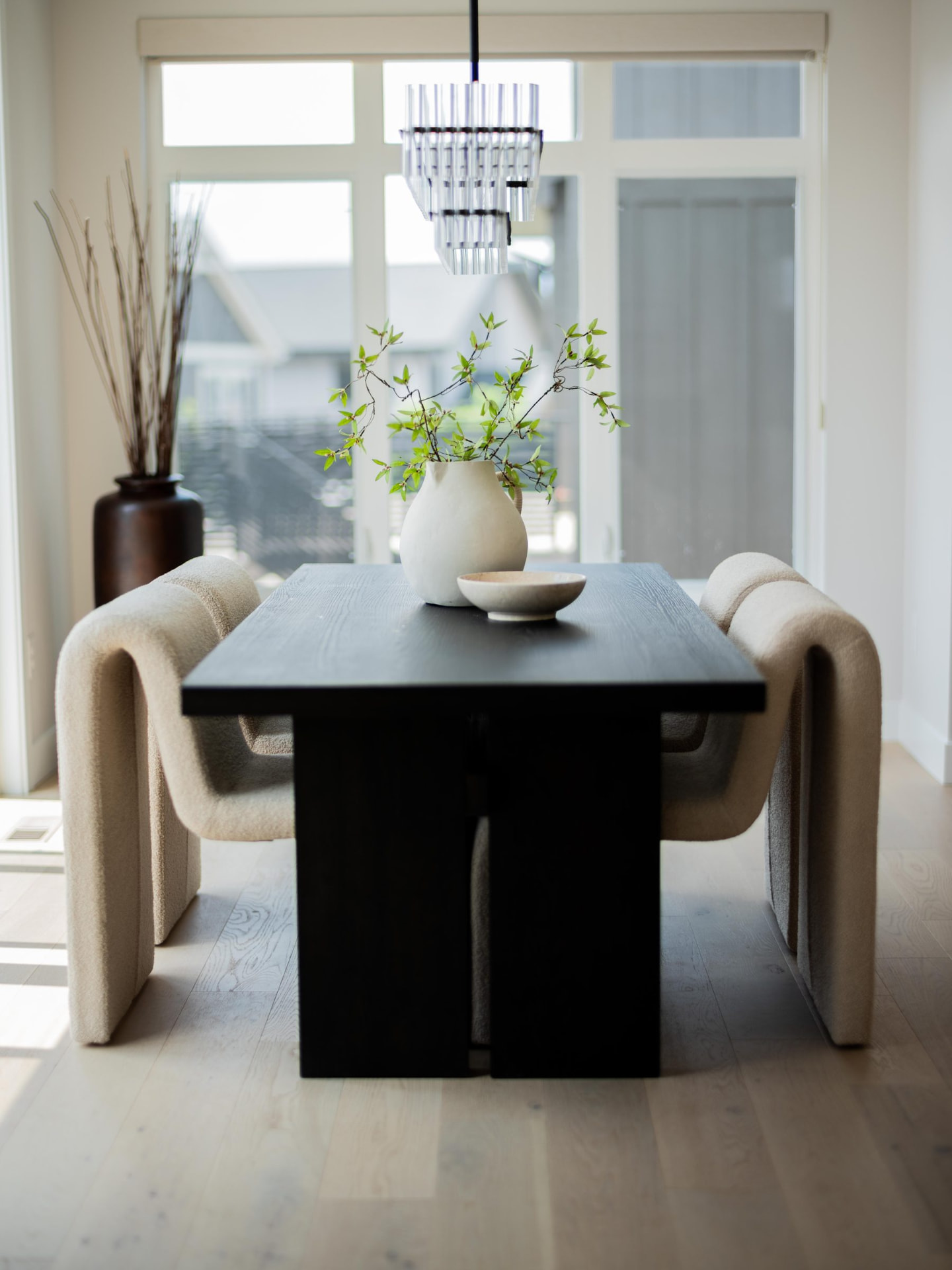 Blackened oak dining table with sculptural bouclé chairs and a fluted glass chandelier against a wall of light