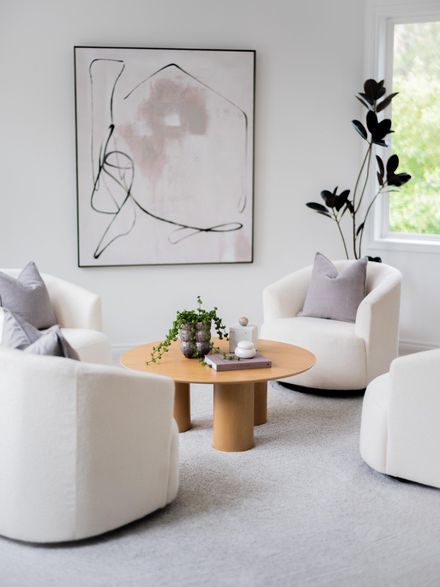 Sitting room with four white swivel chairs, a round oak table and a line-drawing canvas above lilac accents